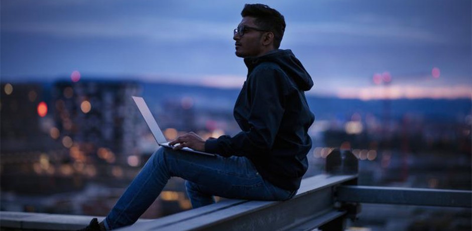 Mann sitzt mit Laptop auf dem Dach