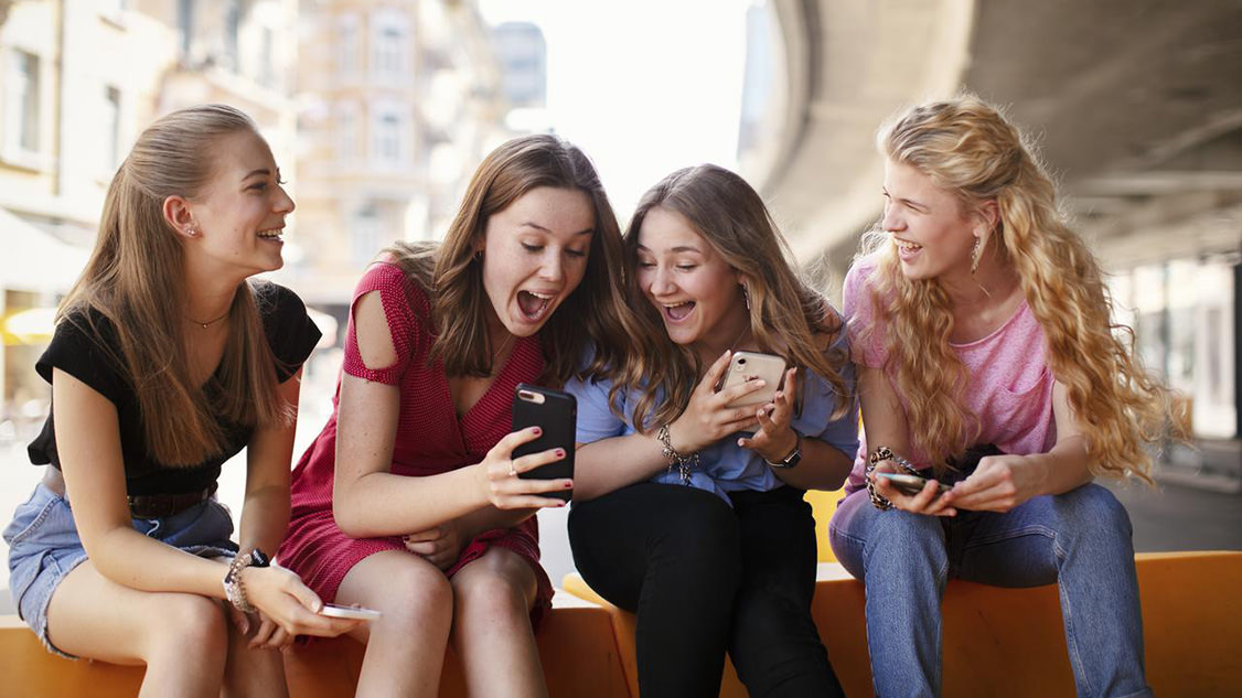 Photo shows young women laughing, looking at smartphones. 