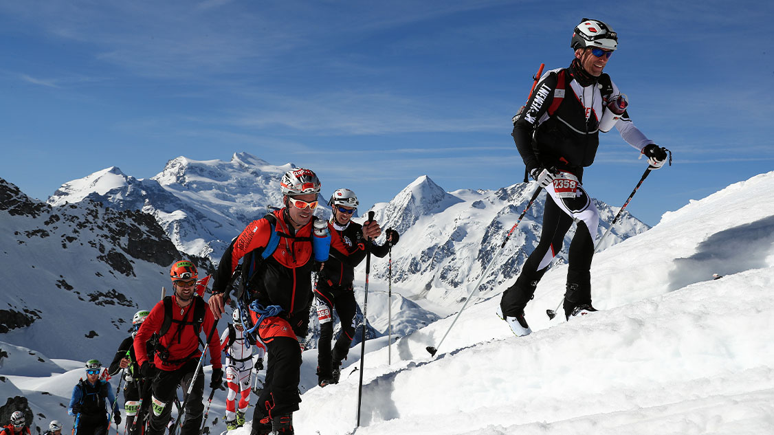 The picture shows athletes on touring skis in the mountains. 