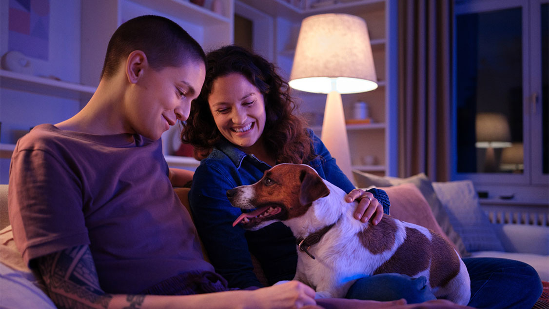 L'immagine mostra una giovane coppia seduta sul divano con il loro cane.