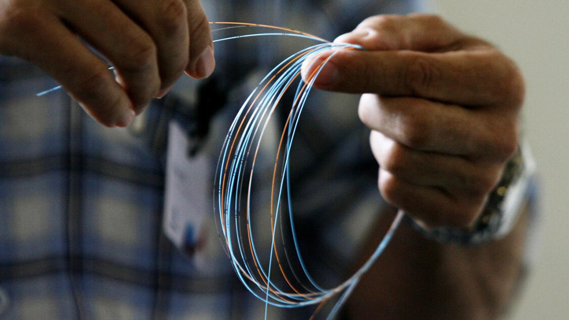 L’image montre deux mains qui tiennent un câble à fibre optique.