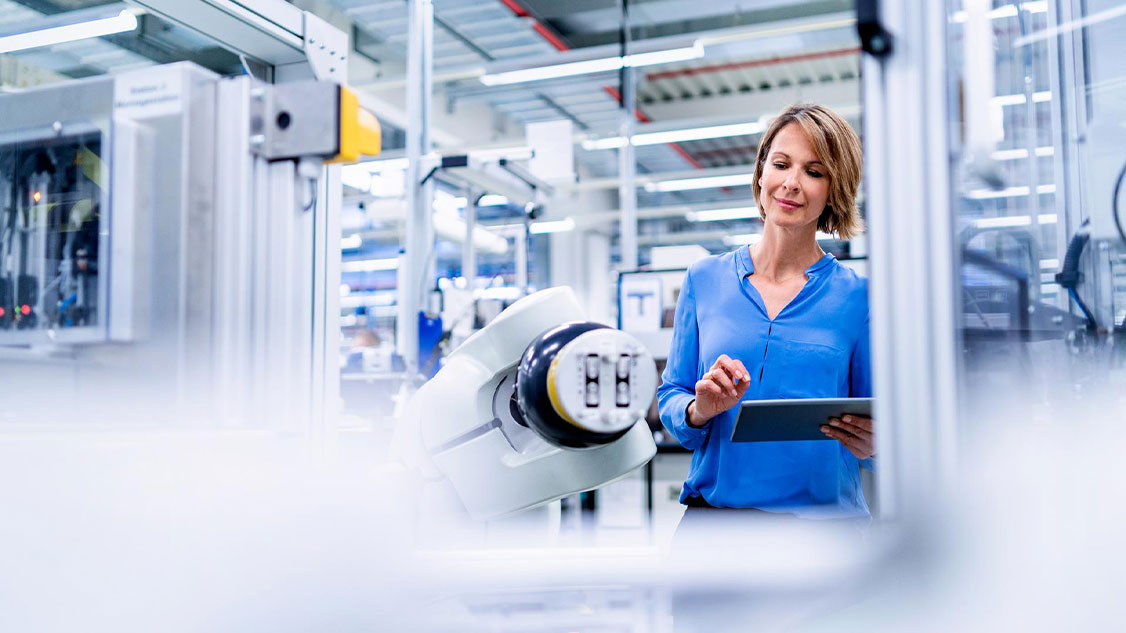 Sur l'image, on voit une femme debout devant un robot dans un atelier de production.