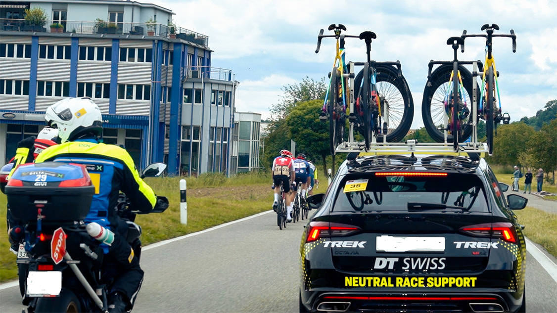 Auf dem Bild ist ein Fahrzeug der Tour de Suisse zu sehen mit zwei auf dem Autodach montierten Velos. 