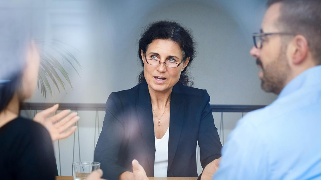 Drei Personen, die an einem Tisch in einem Beratungsgespräch sitzen.