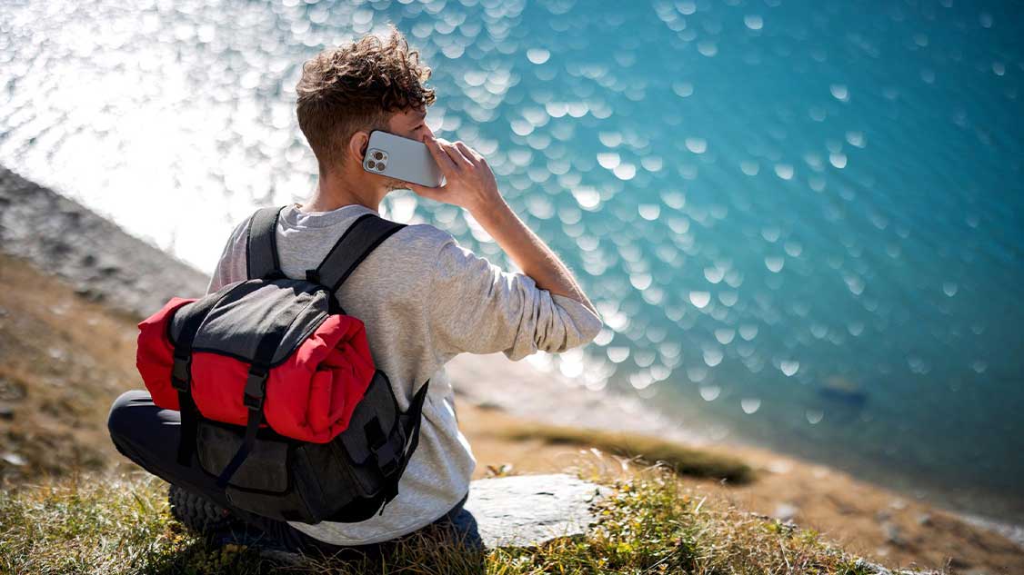 Mann mit Handy steht auf der Klippe, telefoniert und schaut aufs Meer.