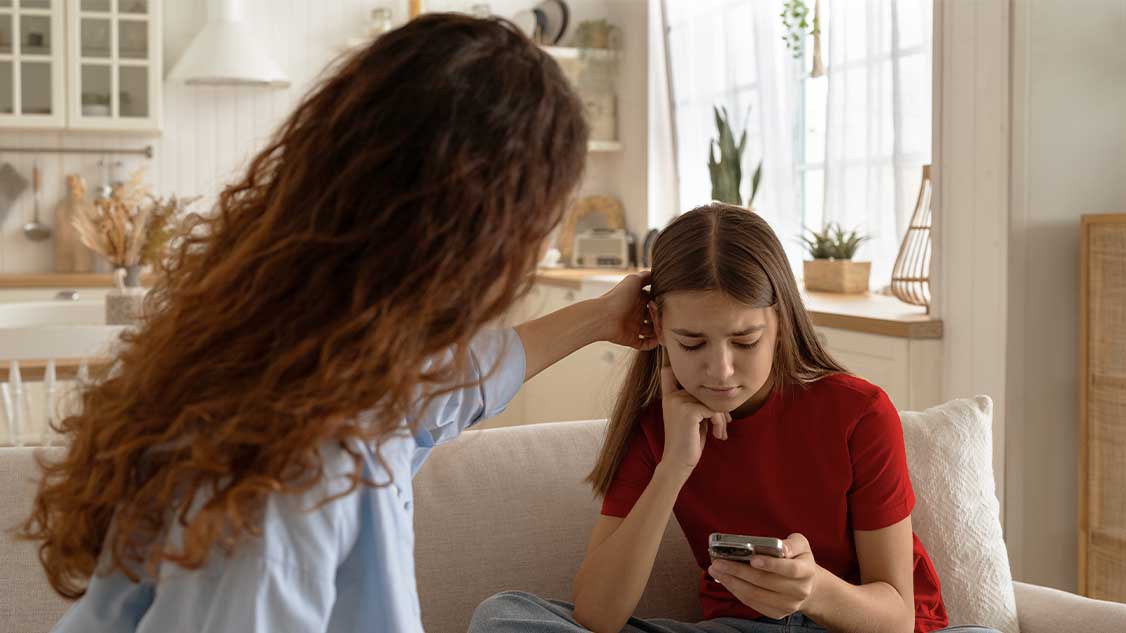 Mutter und Tochter mit Handy auf Sofa