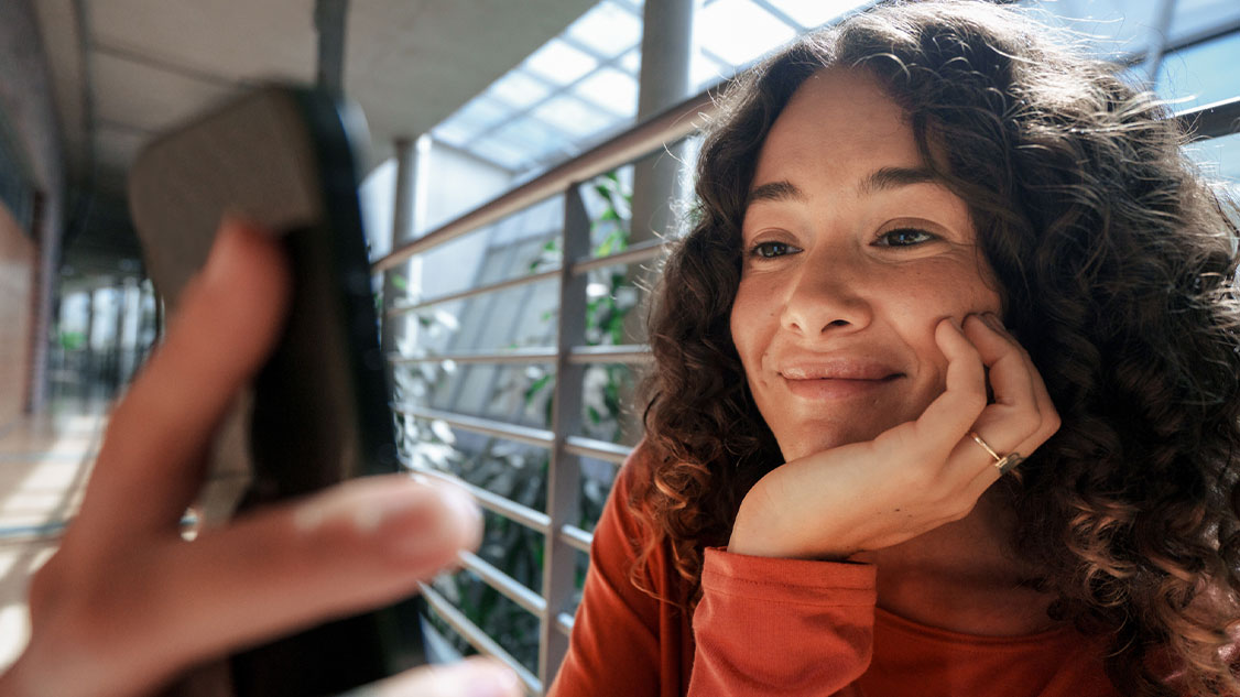 Auf dem Bild ist eine Frau zu sehen, die etwas auf ihrem Smartphone betrachtet.