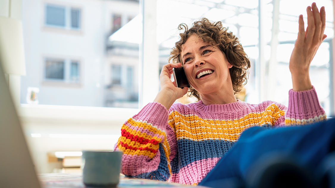 Lächelnde Frau spricht zuhause sitzend am Handy