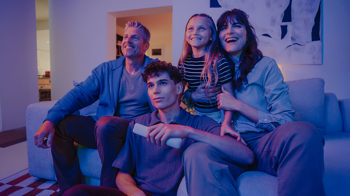 Un homme, une femme et deux enfants assis devant la télévision, heureux en famille