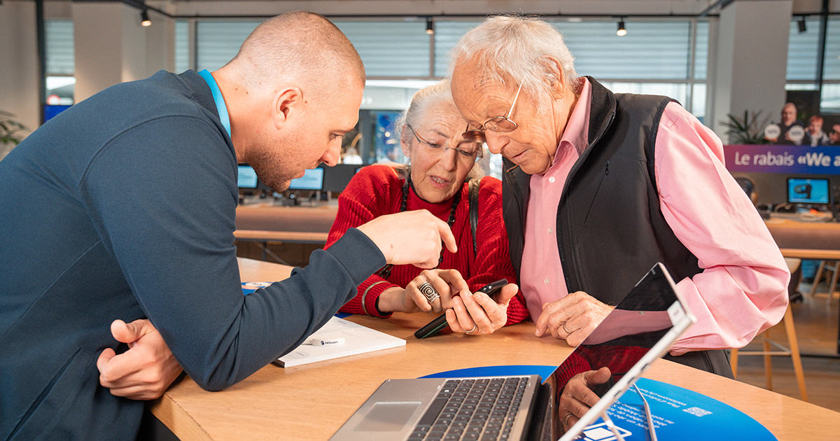 Ein Mitarbeitender im Shop von Swisscom erklärt einem älteren Paar etwas zu einem Smartphone. 