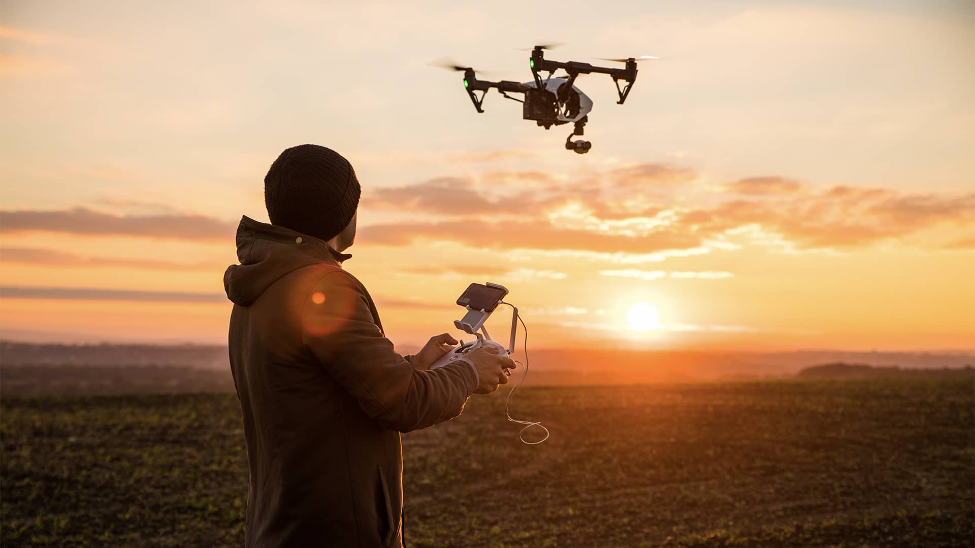 Eine Drohne fliegt im Sonnenuntergang über ein Feld.