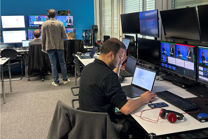 Jan Mathieu und ein Mitarbeiter unterhalten sich im Büro vor einem Bildschirm, der eine Valiant-Schalterhalle und die Login-Maske zeigt.