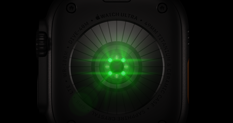 Un Apple Watch Ultra 4 mostrato da dietro, cassa in titanio nero, una serie di sensori rotondi con luci LED verdi che pulsano