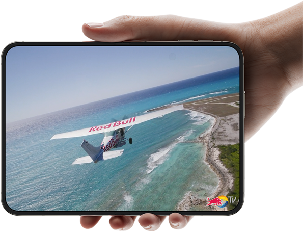 iPhone Duo, held with one hand, opened in horizontal orientation, fully unfolded, interior screen displays a photo of a plane flying over a beach.