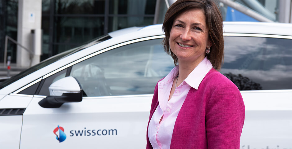Frau mit lachendem Gesicht vor weissem Auto und Gebäude