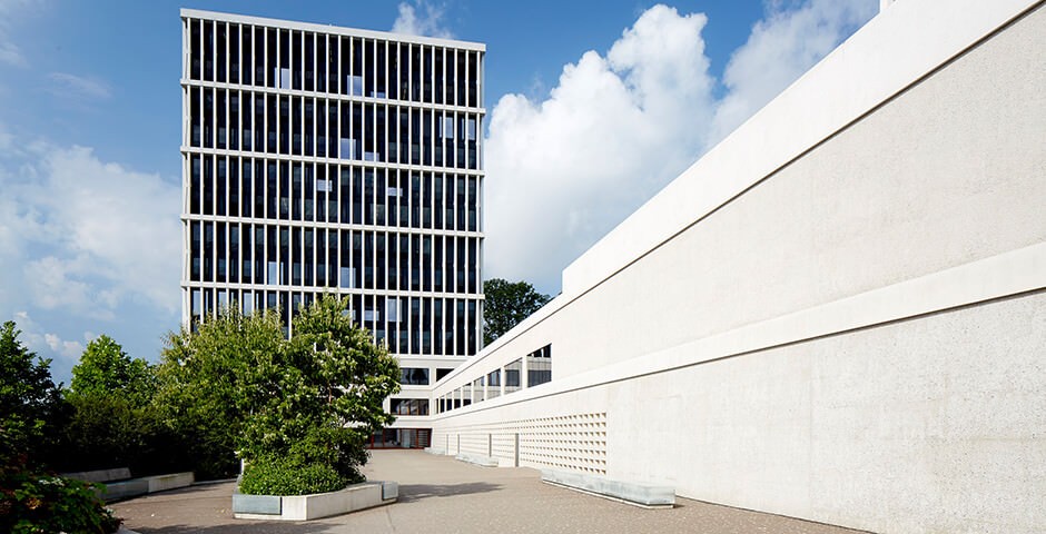 Auf dem Bild ist das Gebäude des Bundesverwaltungsgerichts in St. Gallen zu sehen. Der Himmel ist blau mit weissen Wolken und das Gebäude grau/weiss. Vor dem Gebäude sind Bäume und Büsche zu sehen. Das Gebäude selbst ist ein modernes Hochhaus mit vielen grossen Fenstern.