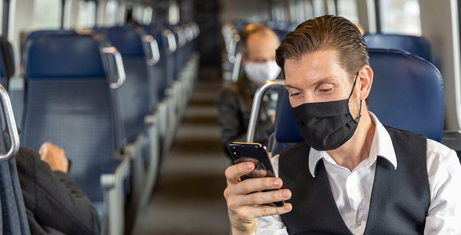 Mann sitzt im Zug, schaut auf sein Smartphone und hört Musik