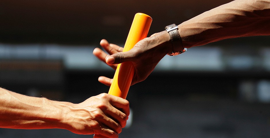 Passage de témoin: le bâton orange passe d’une main à l’autre.