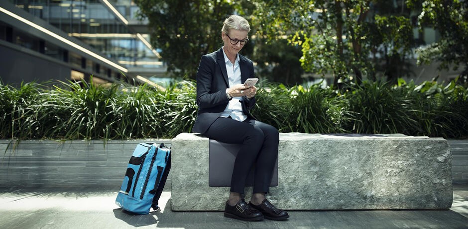 Eine Frau sitzt auf einer Mauer und nutzt ein Smartphone. 