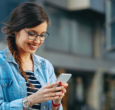 Una ragazza di fronte a un immobile commerciale scrive un messaggio sullo smartphone con il sorriso sulle labbra.