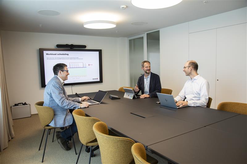 Jan Mathieu und ein Mitarbeiter unterhalten sich im Büro vor einem Bildschirm, der eine Valiant-Schalterhalle und die Login-Maske zeigt.