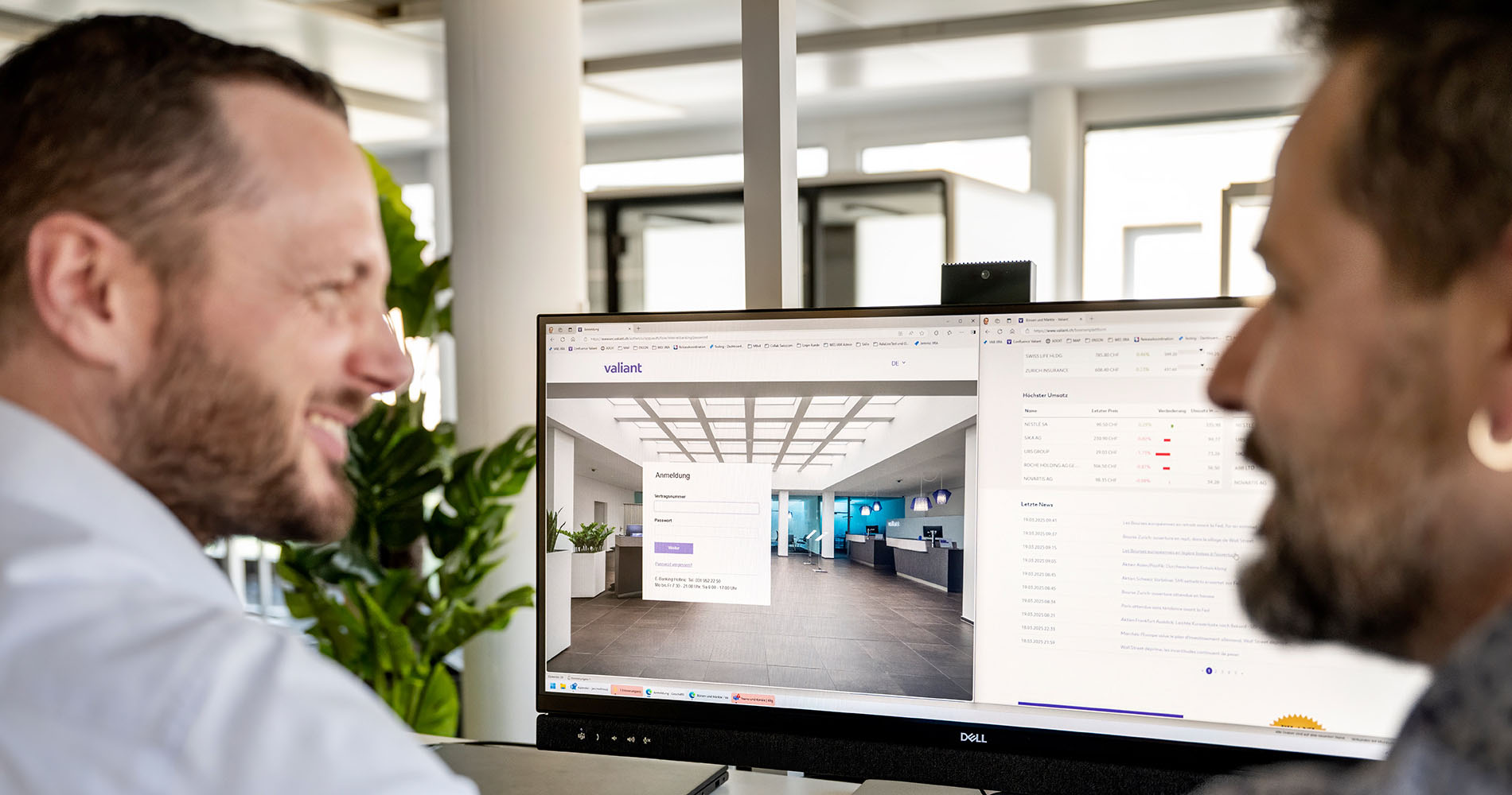 Jan Mathieu und ein Mitarbeiter unterhalten sich im Büro vor einem Bildschirm, der eine Valiant-Schalterhalle und die Login-Maske zeigt.
