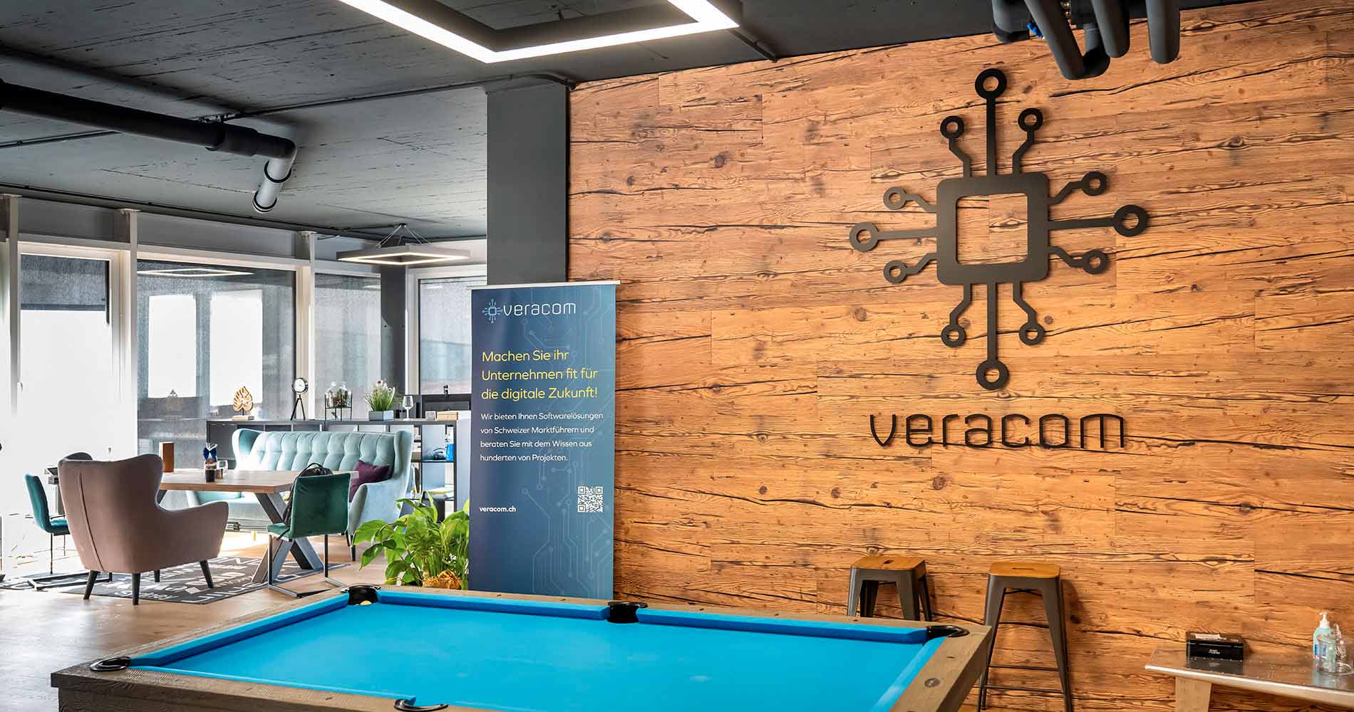 veracom AG offices with wooden wall, logo, sofa, armchair, table and a pool table in the foreground.