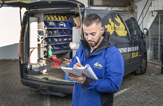 A service technician of the Häsler Group writes down his work hours in the report book in front of his delivery van.