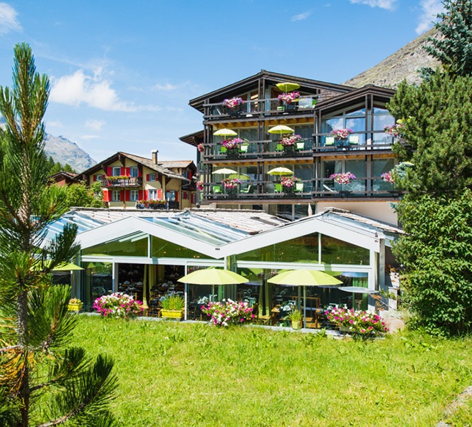 The chalet-style Hotel Zurbriggen, surrounded by green meadows and Alpine scenery. 