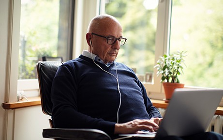 Un uomo meno giovane naviga sul laptop e indossa le cuffie